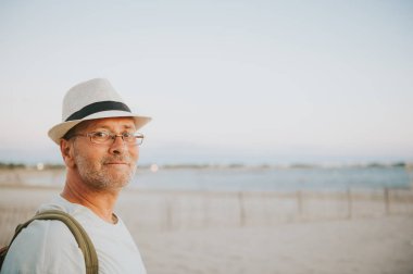 Şapka, gözlük ve sırt çantası giyiyor yakışıklı yaz tatilde deniz kenarında