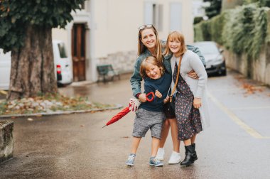 İki çocuklu genç mutlu anne, küçük erkek ve kız, dışında taze yağmurlu bir günde oynarken. Şık aile açık havada eğleniyor