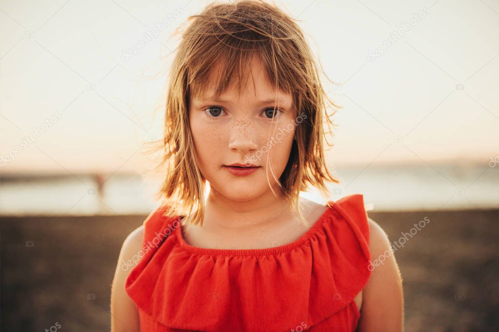 Close up portrait of sweet little girl with short bob haircut resting by the sea at sunset