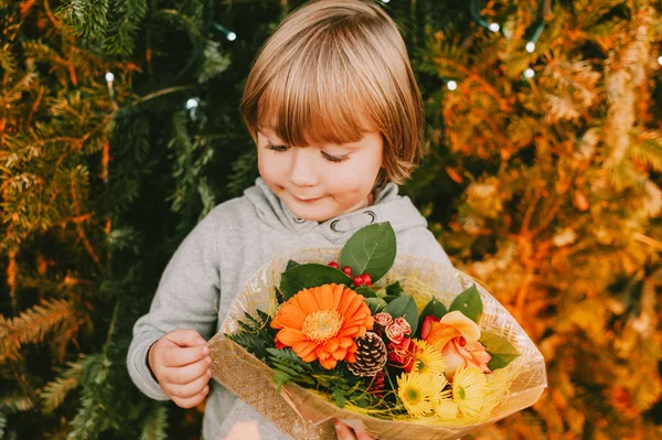 クリスマスツリーの横に立って クリスマスの花の花束を保持かわいい男の子の肖像画 — ストック写真