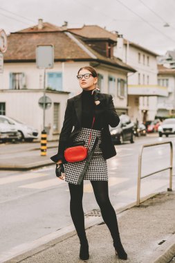 Sokakta poz veren, siyah ceketli, etekli, şık bir kadının açık hava moda portresi.
