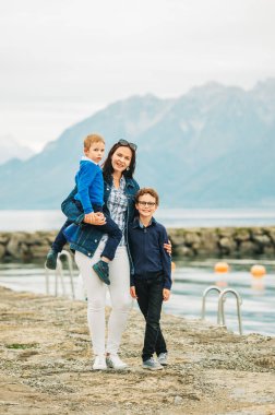 Göl kenarında yürüyen iki oğlu olan mutlu bir anne, aile gezisi.