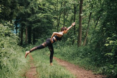 Yaz ormanlarında yoga yapan, siyah taytlı, formalı genç bir kadın.