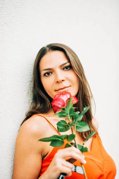 Portret Atrakcyjnej Kobiety Trzymającej Różowy Kwiat Noszącej Pomarańczowe Ubrania — Zdjęcie stockowe