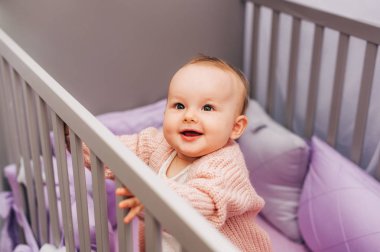 Gri beşikte mor çarşafla oynayan sevimli bir kızın portresi.