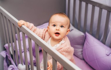 Gri beşikte mor çarşafla oynayan sevimli bir kızın portresi.