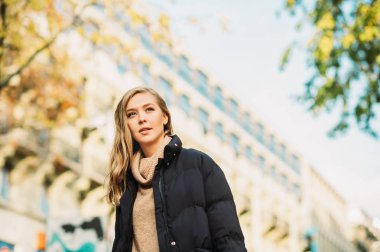 Street fashion portrait of young beautiful woman wearing beige roll neck pullover and black padded coat