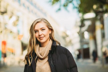 Street fashion portrait of young beautiful woman wearing beige roll neck pullover and black padded coat