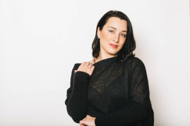 Siyah kazak giyen, beyaz arka planda poz veren güzel esmer kadının stüdyo portresi.