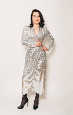 Stüdyo boyunda, beyaz arka planda poz veren gümüş pullu elbise giyen güzel esmer kadın portresi.