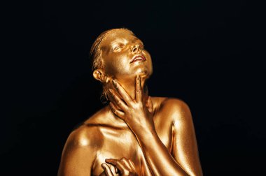 Şehvetli kadının portresi altın boyayla kaplı, siyah arka planda poz veriyor, gözleri kapalı.