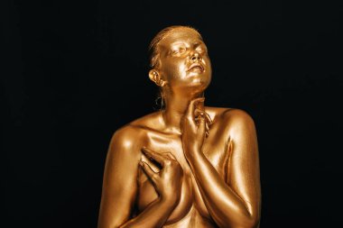 Şehvetli kadının portresi altın boyayla kaplı, siyah arka planda poz veriyor, gözleri kapalı.