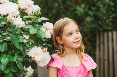 Açık havada küçük sevimli bir kızın portresi, bahçede güllerle güzel bir çocuk.