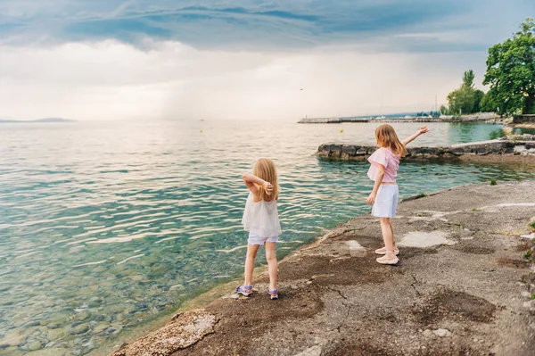 小女孩们在湖边玩耍 孩子们在外面玩得很开心 把石头扔到水里 回头看 — 图库照片