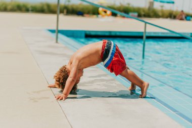 Havuz kenarında baş aşağı duran çok komik bir çocuk.