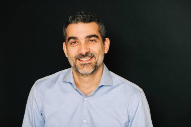 Resmi mavi gömlek giyen, siyah arka planda poz veren yakışıklı bir adamın stüdyo portresi.