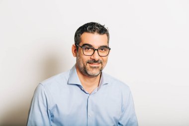 Resmi mavi gömlek ve gözlük takan, beyaz arka planda poz veren yakışıklı bir adamın stüdyo portresi.