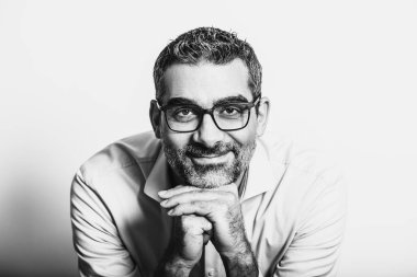Mavi gömlek ve gözlük takan, ellerine yaslanan, beyaz arka planda poz veren yakışıklı bir adamın siyah beyaz portresi.
