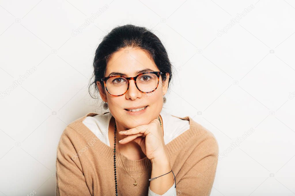 Studio portrait of beautiful brunette woman, wearing glasses, leaning on a hand, posing on white background