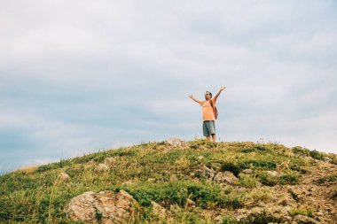 Man standing on the top of the hill, wearing backpack, arms wide open