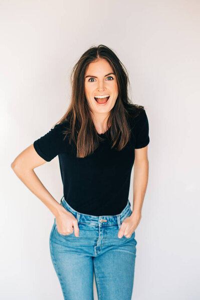Indoor portrait of beautiful laughing woman, wearing black t-shirt and high waist jeans, posing on white background