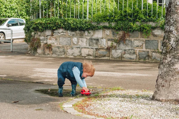 可笑的小孩在水坑里玩玩具车 — 图库照片