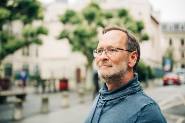 Şehir caddesinde gözlük ve mavi kazak giyen orta yaşlı bir adamın açık hava portresi.