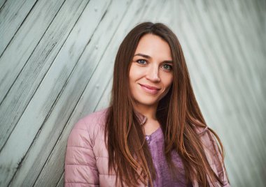 Duvara dayanmış, uzun kahverengi saçlı güzel bir kadının açık hava portresi.