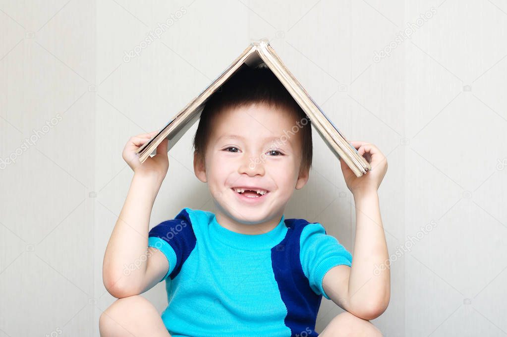 Happy boy with book on head making roof