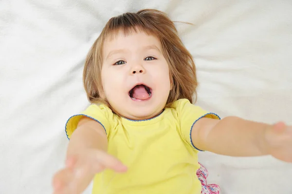 Glad rolig liten flicka med händerna upp liggande på sängen — Stockfoto