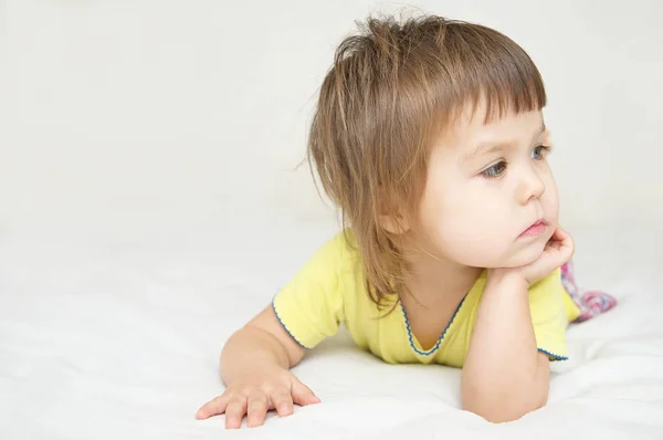 Thoughtful child, sad little girl lying on bed looking away isolated — Stock Photo, Image