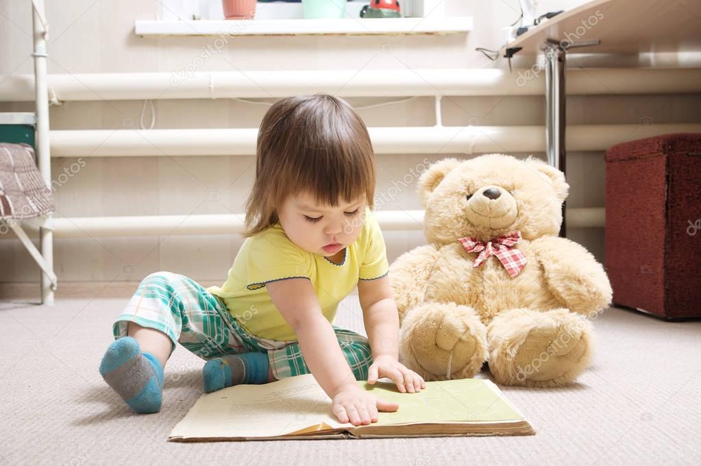 little girl reading book indoor in her room on carpet with toy Teddy bear, child playing school, children education and development, happy childhood