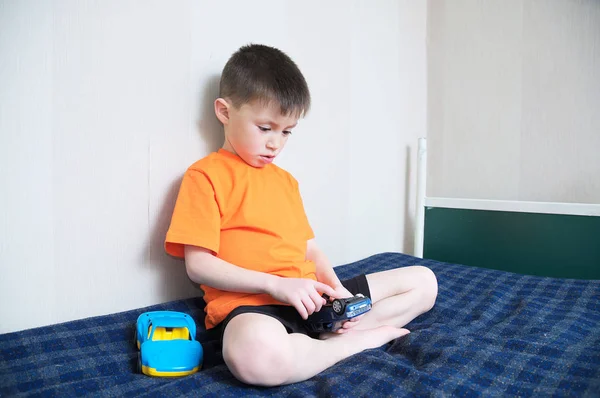 Chłopiec gry samochód gry, chłopiec bawi się zabawkami, siedząc na łóżku kryty, dziecko trzymając dwa autka w domu sam — Zdjęcie stockowe