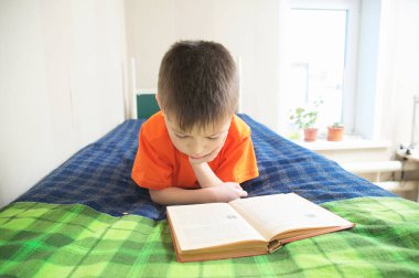 Çocuk eğitimi, çocuk okuma kitabı yatakta, kitap ile eğitim kavramı, hikaye kitabı ilginç gülümseyen çocuk portre yalan