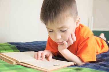 Çocuk eğitimi, çocuk okuma kitabı yatakta, kitap ile eğitim kavramı, hikaye kitabı ilginç gülümseyen çocuk portre yalan