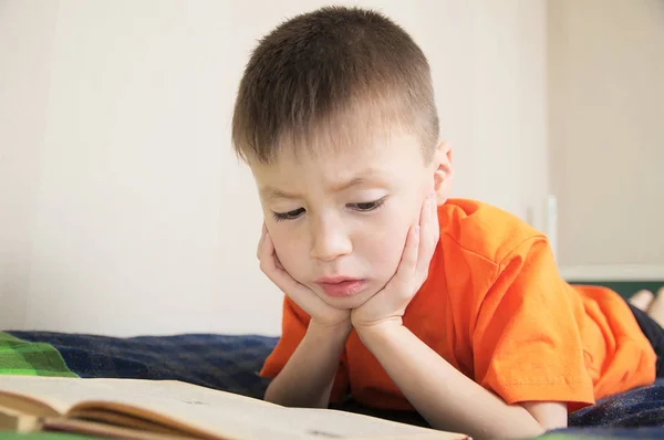 Kindererziehung, Kinderlesebuch im Bett liegend, Jungenporträt mit Buch, Bildungskonzept, interessantes Bilderbuch — Stockfoto