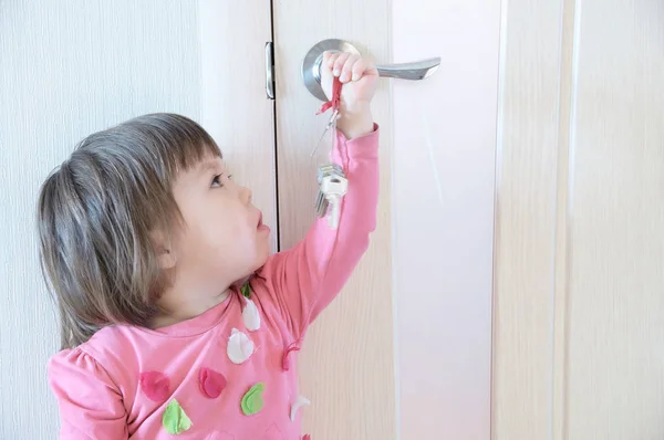 Kind spelen met sleutels vergeten door ouders in het sleutelgat van de deur. Kinderen veiligheid en binnenlandse veiligheidsconcept. — Stockfoto