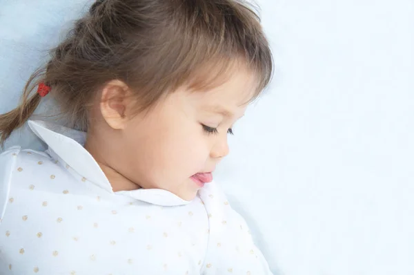 Playful little girl portrait looking down with interest lying on white blanket — Stock Photo, Image