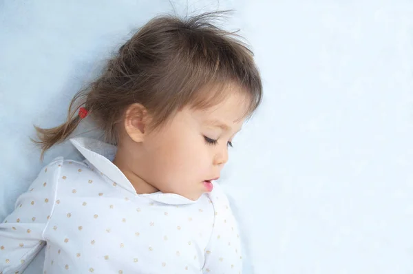 Little girl portrait looking down with interest lying on white blanket — Stock Photo, Image