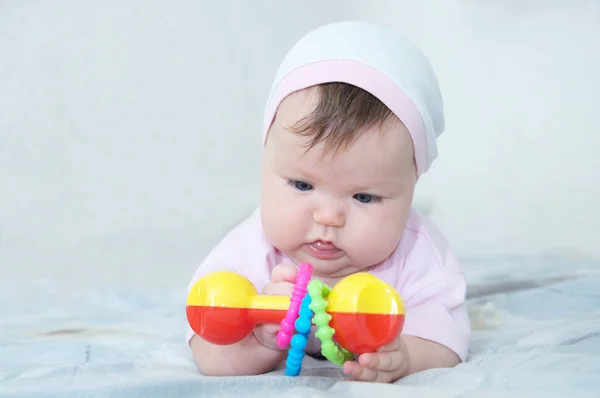 Tidiga hjärnans utveckling. koncentrerad liten baby flicka leker med skallra liggande på sängen — Stockfoto