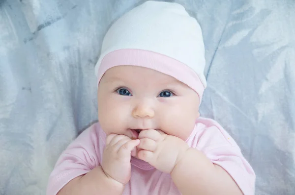 Baby flicka stående med handen i munnen liggande på sängen — Stockfoto