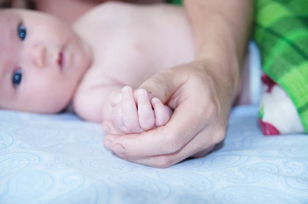 Father holding baby hands, dad and infant lying together on bed — Stock Photo, Image