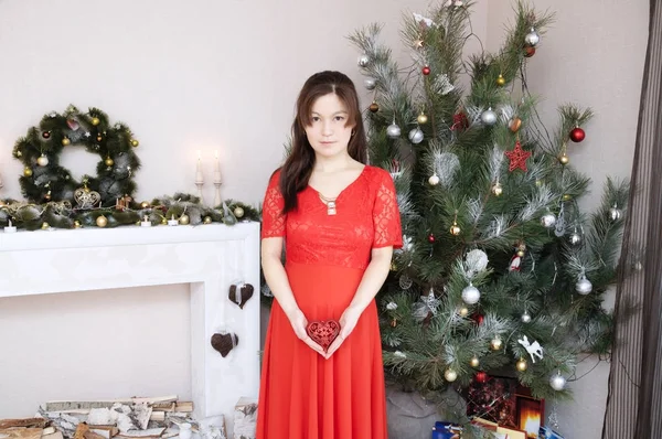 Zwangere vrouw in rode jurk portret in interieur bedrijf kersthart op haar buik — Stockfoto