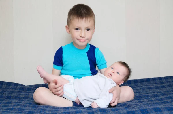 Hermano sosteniendo a la pequeña hermana recién nacida acostada en sus piernas en casa, hermanos juntos — Foto de Stock