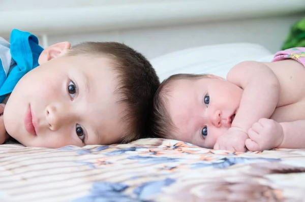 Irmão e irmãzinha recém-nascida deitados na cama em casa juntos — Fotografia de Stock