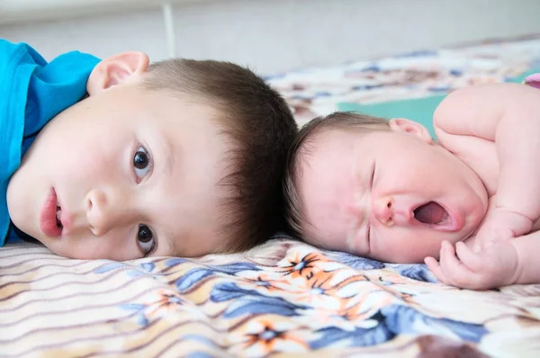 Hermano y hermanita recién nacida bostezando tumbados en la cama en casa juntos — Foto de Stock