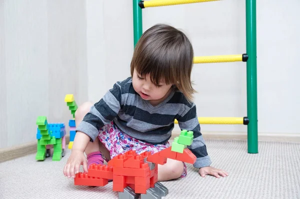 Niña jugando con figuras de dinosaurios hechas por juguetes de bloques de construcción de plástico — Foto de Stock