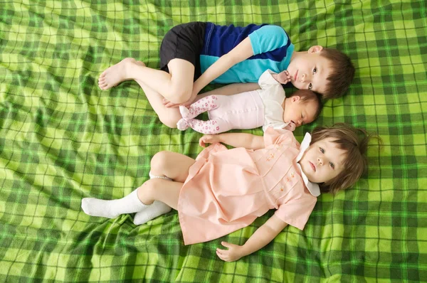Drei Geschwisterkinder liegen in großer Familie auf dem Bett, umarmen und umarmen sich liebevoll — Stockfoto