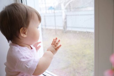 Biraz güneş ışığı için özlem pencere bakarak çocuk. merak childness. pembe elbiseleri bir yıl camda meraklı çocuk evde yağmurlu bir gün eski meraklı bebek kız