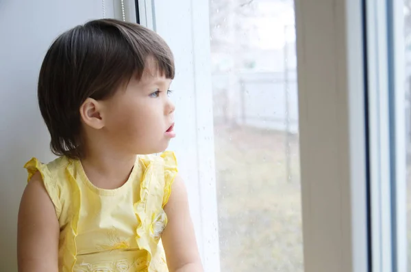 小女孩望着窗外渴望阳光 好奇心 Childness 沉思的孩子坐在家里在雨天 — 图库照片